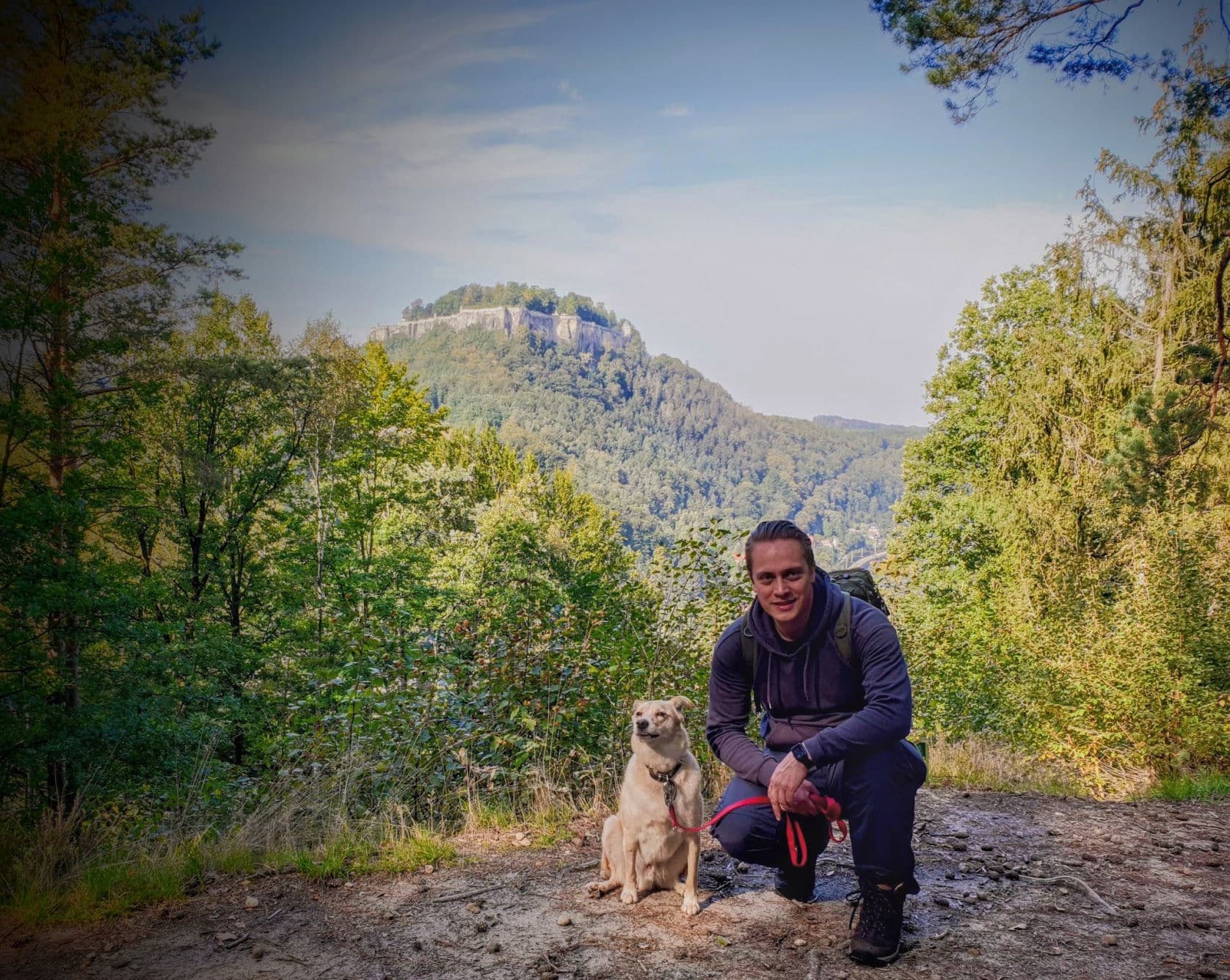Sebastian kniet auf einem Waldweg neben einem hellen Hund